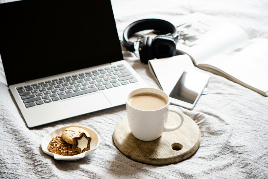 Real home workplace, laptop with cup of coffee with cookies on bed with cozy blanket
